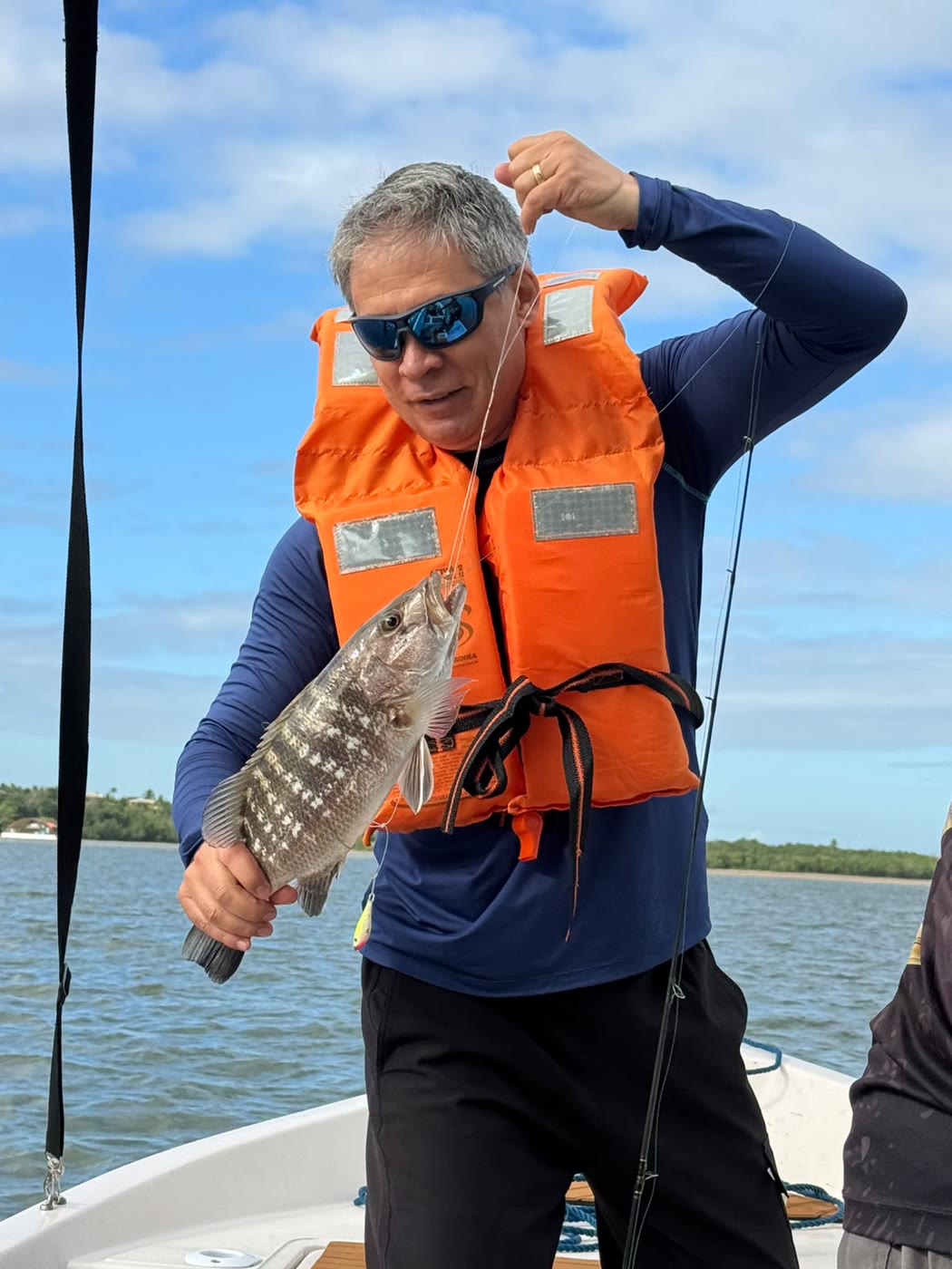 Pescador de colete laranja com um peixe fisgado na isca