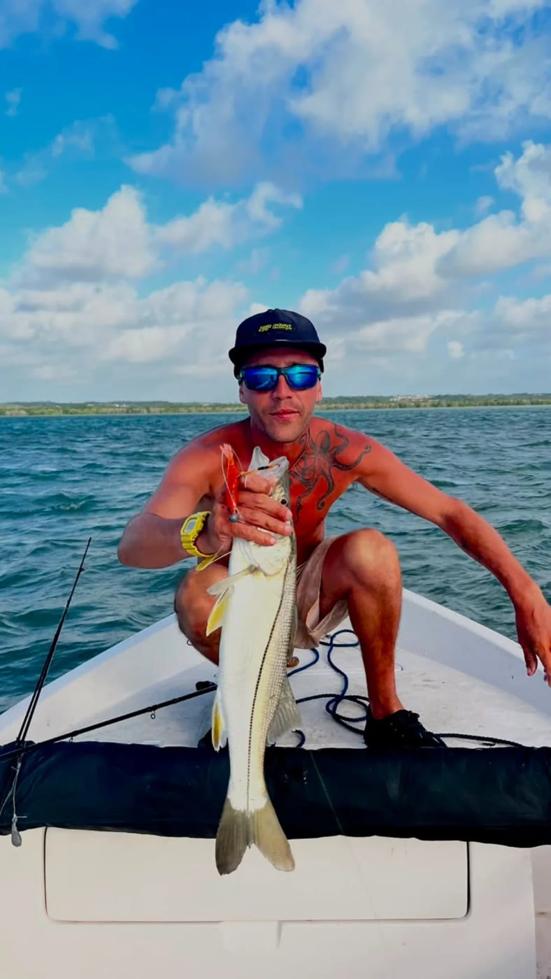 Pescador agachado na proa com um robalo