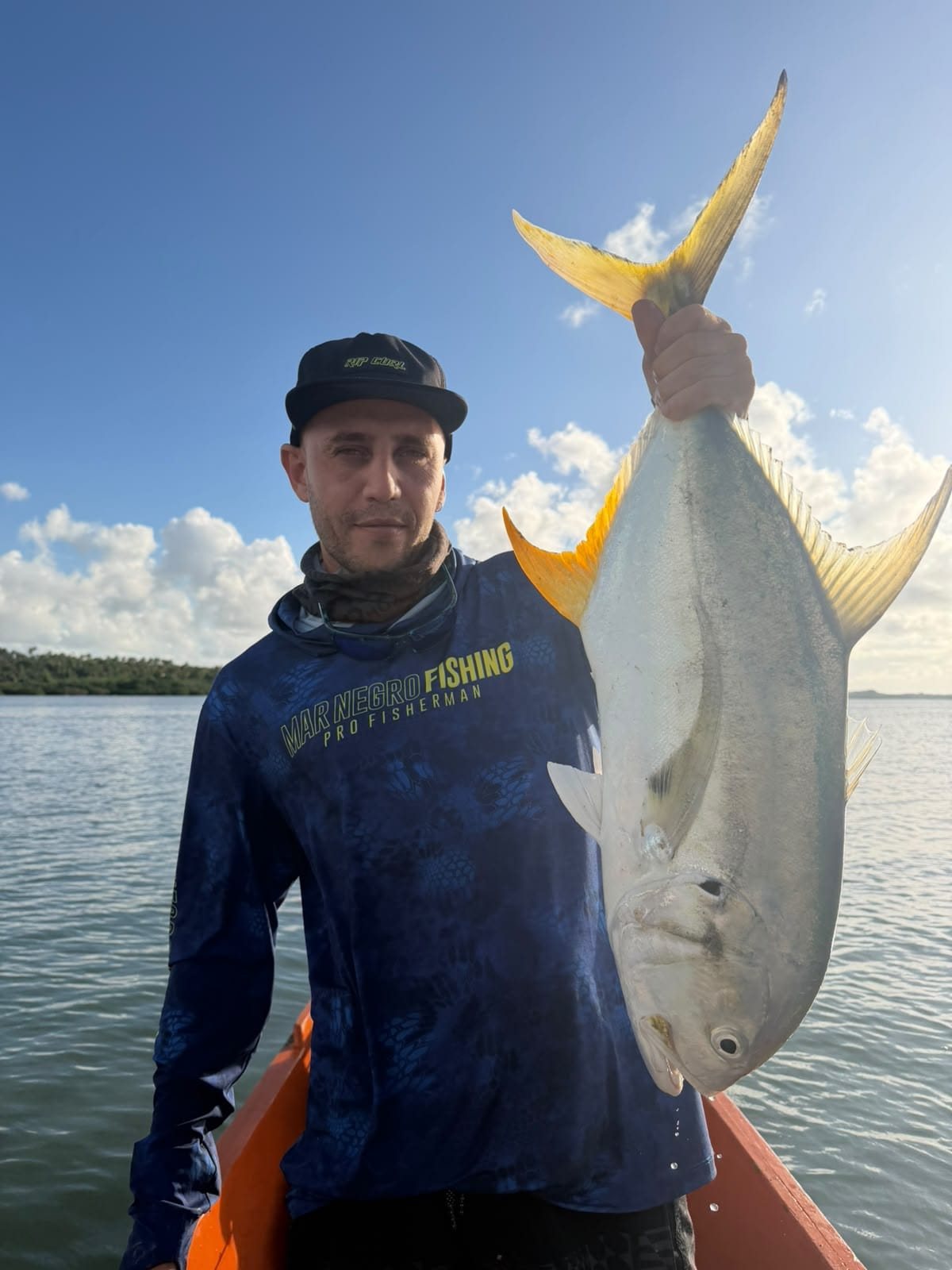 Pescador de boné segurando um xaréu de rabo amarelo