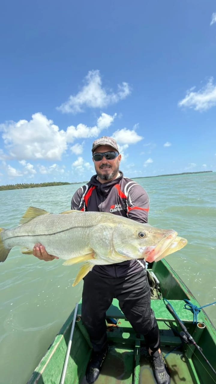 Pescador de óculos escuros com um robalo grande no barco verde